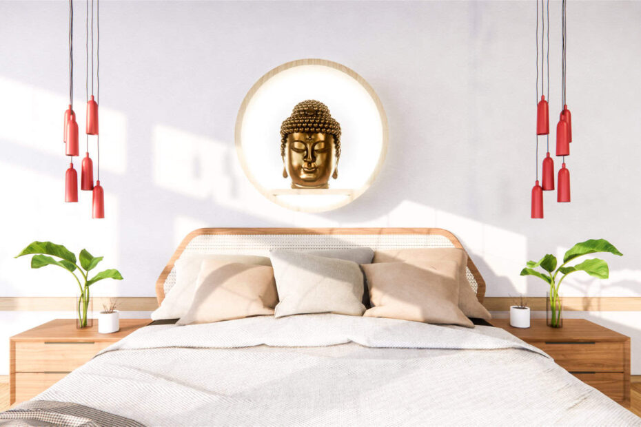 Chambre moderne avec un lit en bois, une literie neutre, deux plantes et une tête de Bouddha décorative sur le mur. Des suspensions rouges sont suspendues symétriquement des deux côtés.